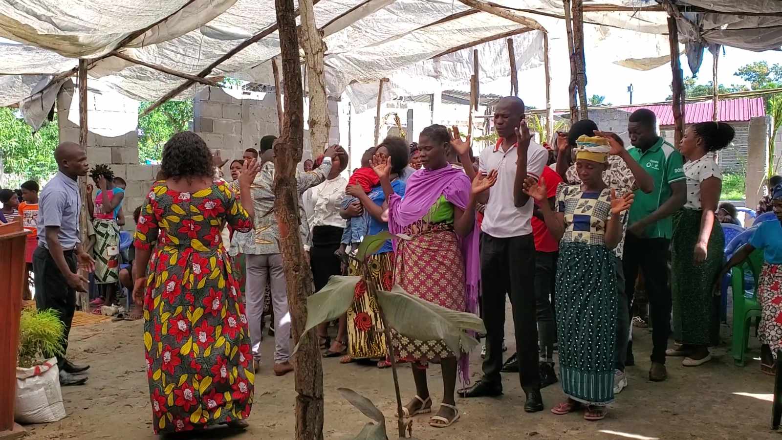 A partner church gathered with hands raised in worship and prayer in their unfinished building in Mozambique.