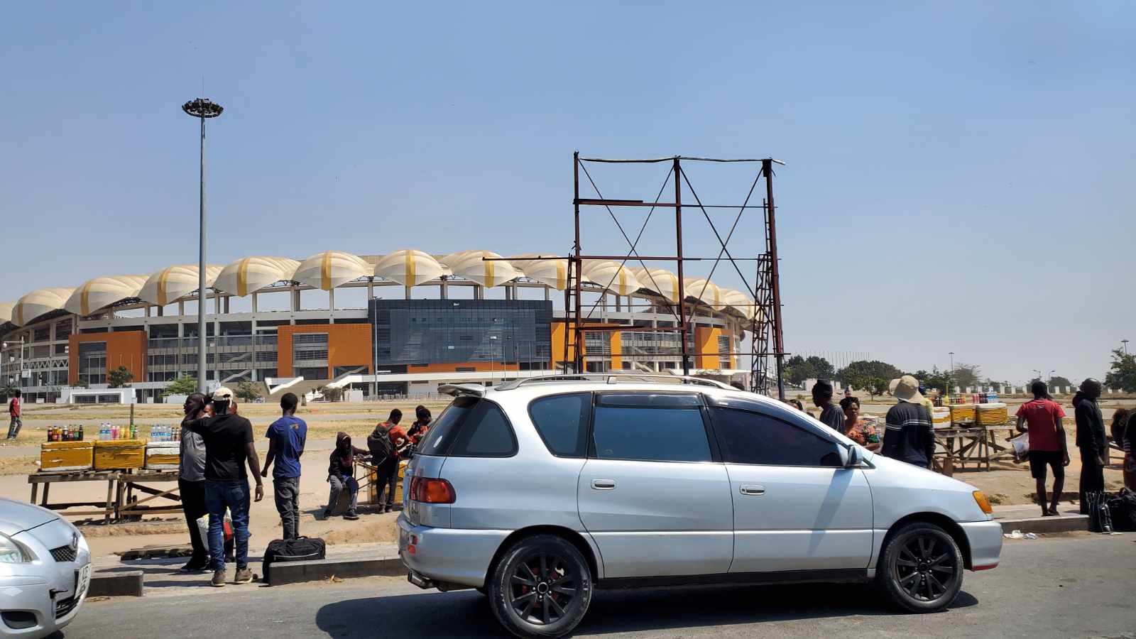 A busy roadside with vendors and cars in front of the National Heroes Stadium in Lusaka, Zambia